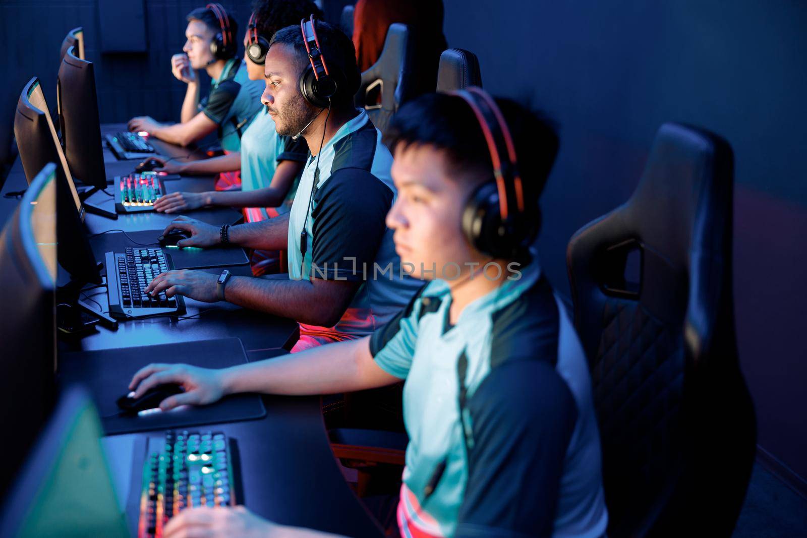 Group of concentrated video game club participants in modern headsets sitting in row and playing computer game indoors