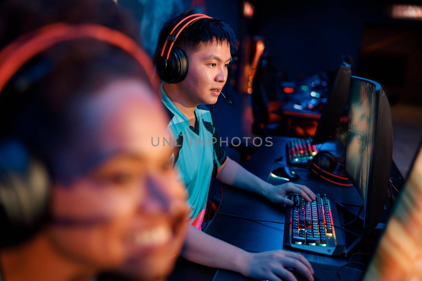 Concentrated Asian esports gamer wearing headset looking at PC monitor while practicing in online arena in contemporary e-sports club