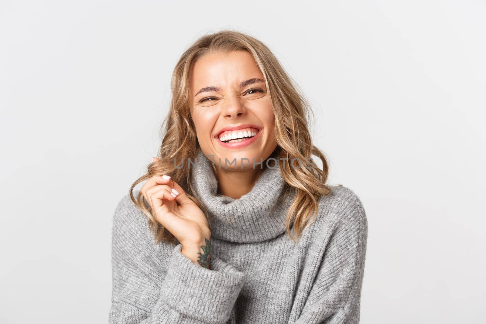 Close-up of attractive happy woman in grey sweater, laughing and smiling, express positivity, standing over white background.