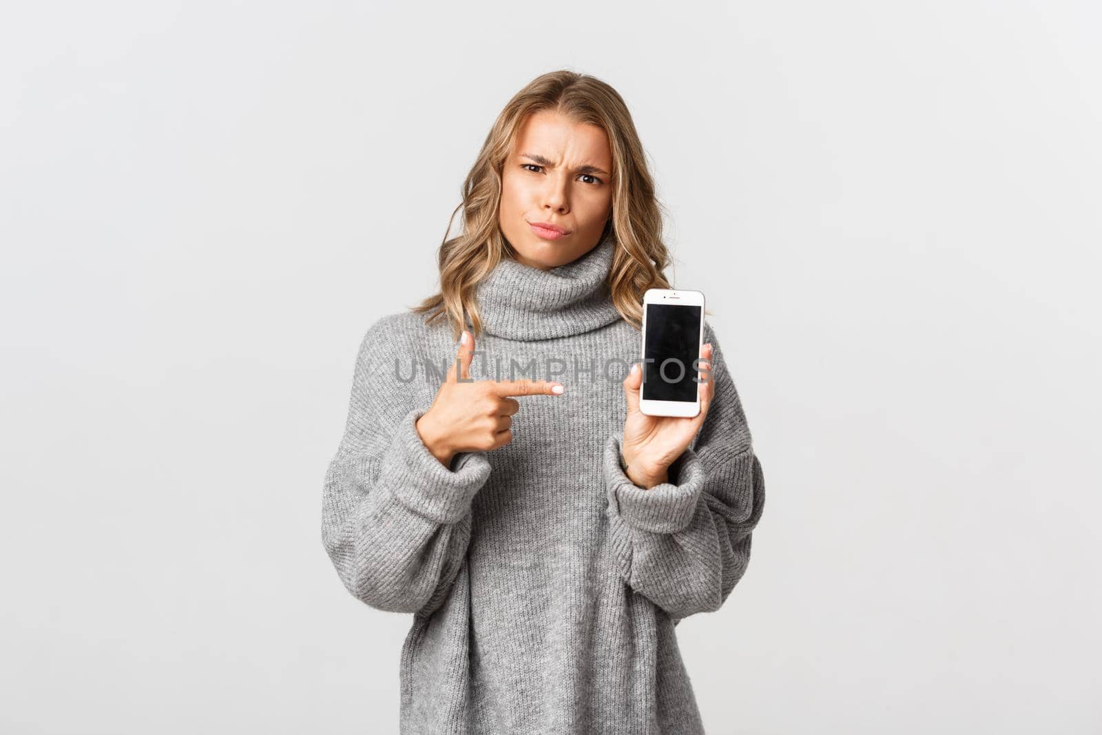 Portrait of angry girl pointing finger at smartphone, showing something disappointing and waiting for explanation, standing over white background by Benzoix