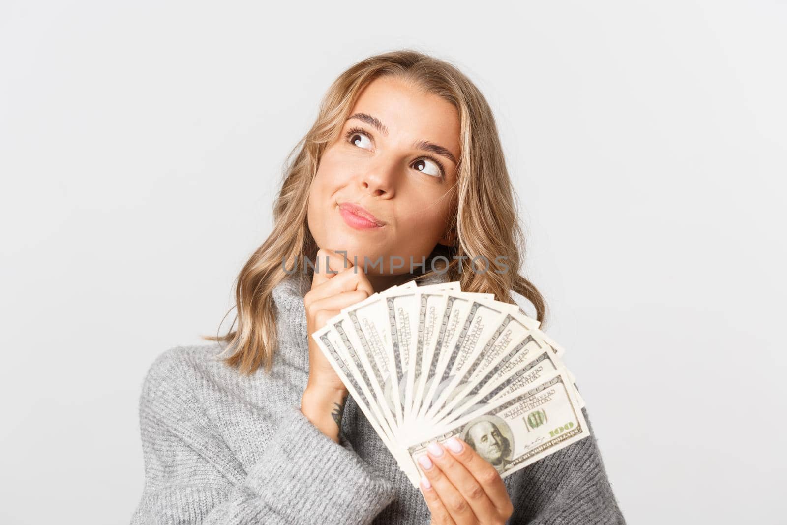 Close-up of thoughtful blond girl with money, looking at upper left corner, dreaming about shopping, white background.