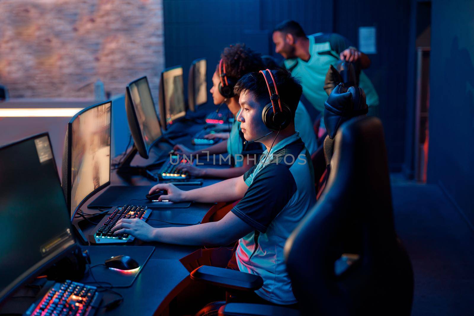 Side view of concentrated Asian professional gamer participating in online cyber games tournament while sitting at pc gaming club