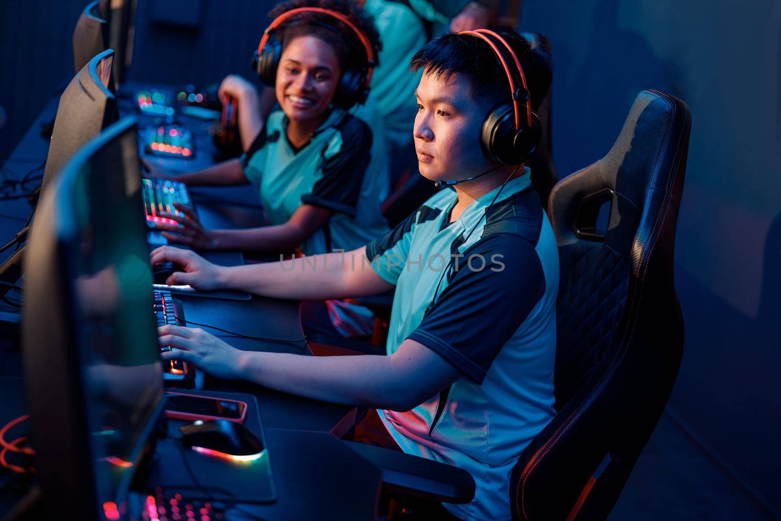Concentrated Asian male cybersport gamer wearing headphones playing online video game while participating in esports tournament in internet cafe