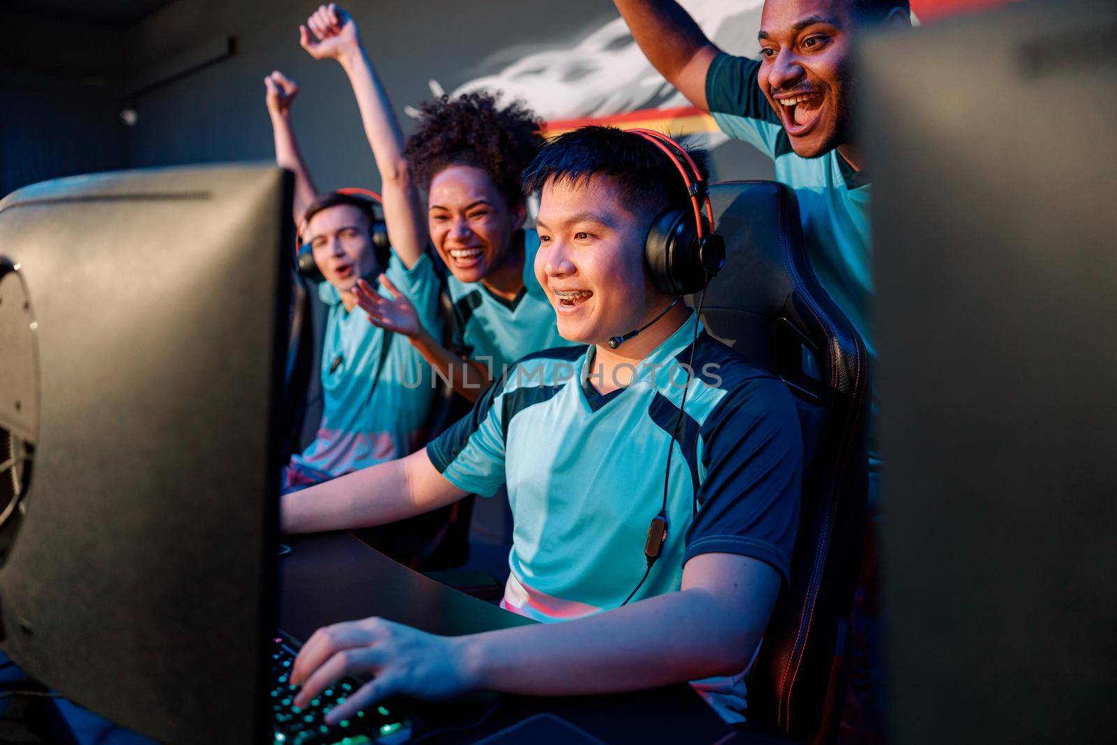Happy multiracial cybersport team celebrating success, raising hands up while participating in esports tournament in gaming club