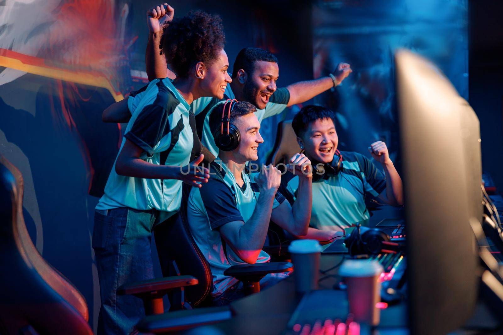 Multiracial cybersport gamers expressing success while raising hands up and smiling during participation in esports tournament in computer club