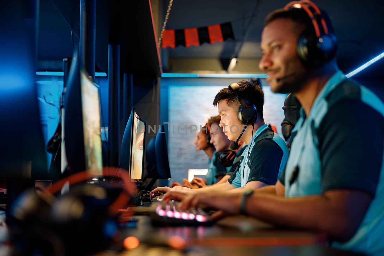 Selective focus on determined Asian cybersport player participating in online video games competition with blurred team members on background