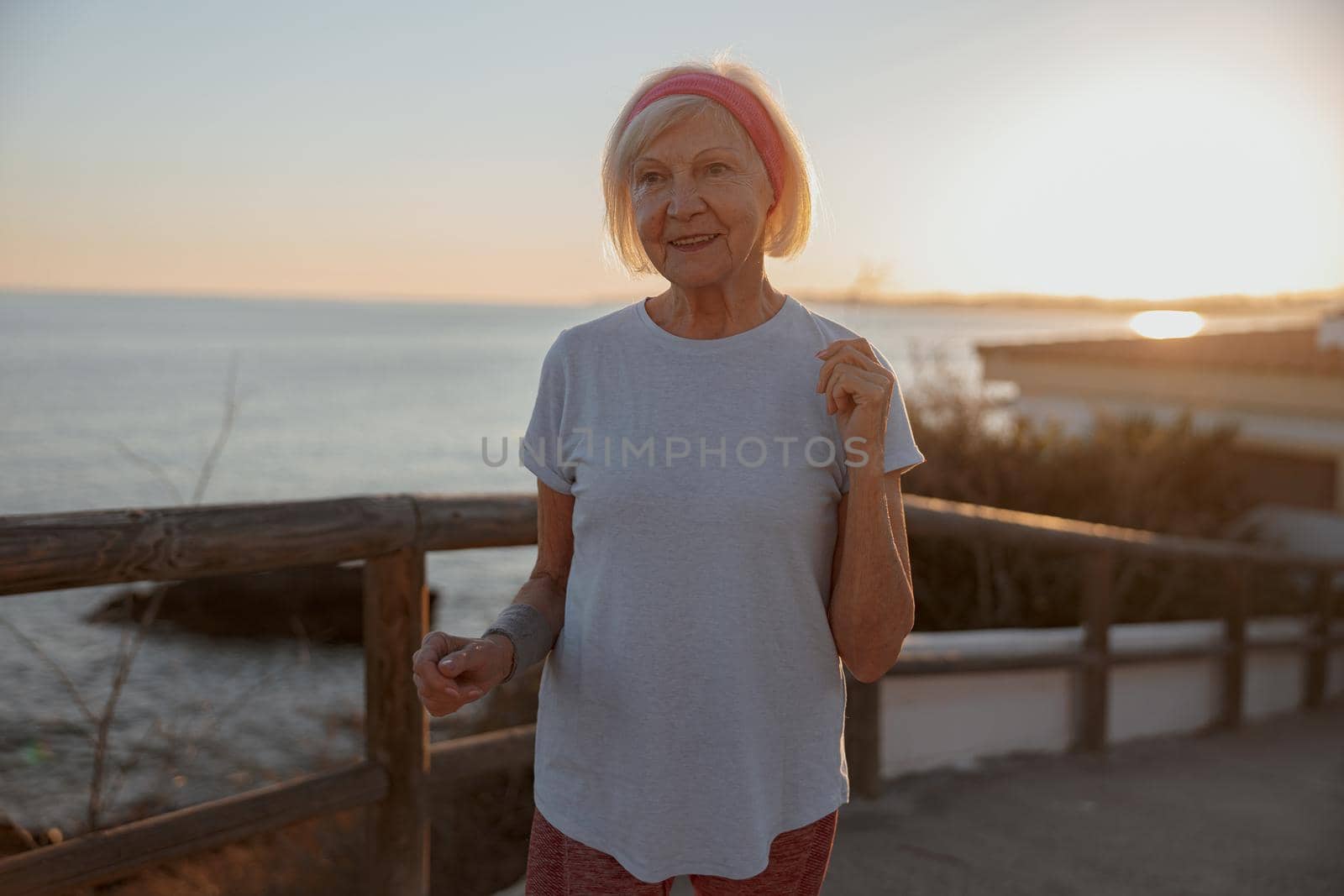 Caucasian good looking senior woman keeping fit and healthy during walking exercises in public park at evening sunset