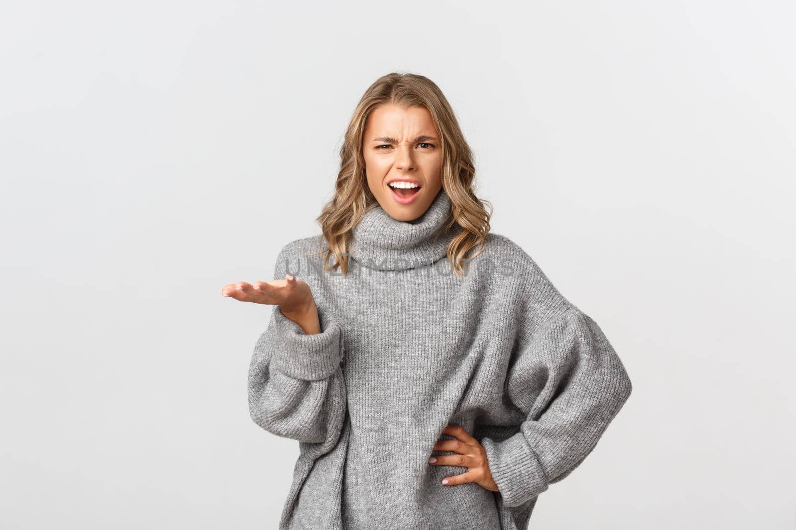 Image of frustrated and bothered blond woman in grey sweater need answers, raising hand and frowning, standing over white background.