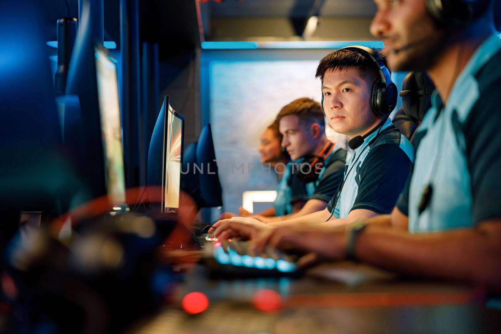Team of professional esports gamers with concentrated Asian man in focus playing in video games on cyber tournament indoors