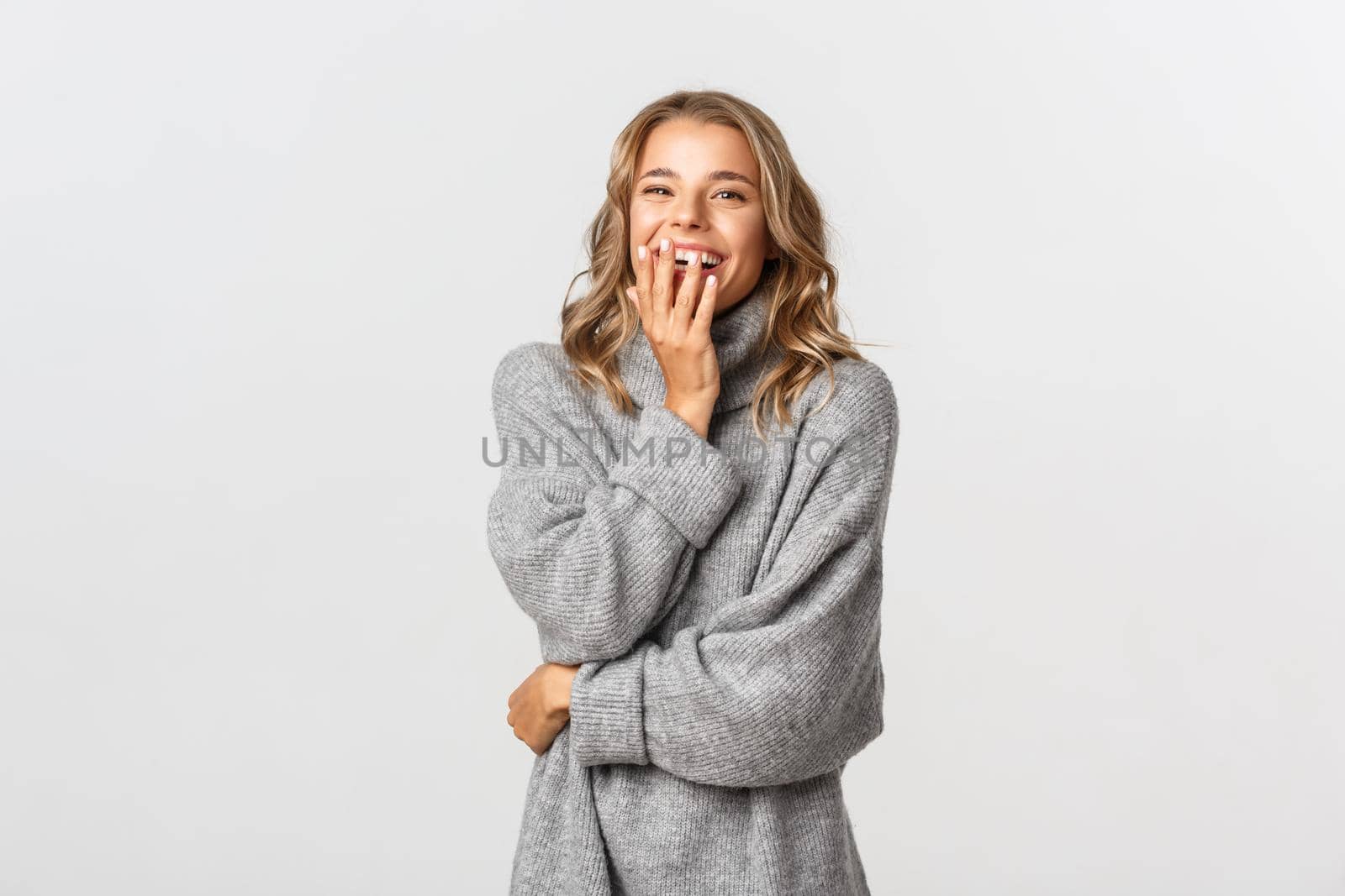 Image of attractive blond girl in casual clothing, laughing and cover mouth coquettish, standing against white background by Benzoix