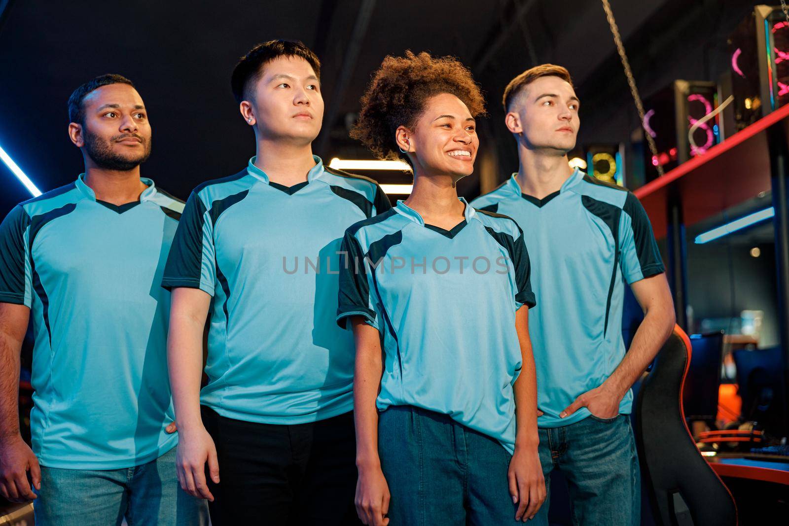 Group of young happy gamers in blue t-shirts looking side and standing like heroes in computer club