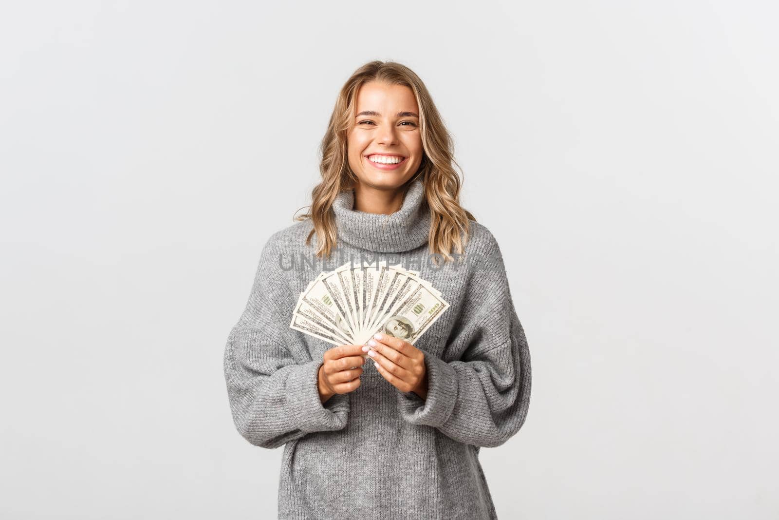 Close-up of happy beautiful woman in grey sweater, holding huge amount of cash, receiving money and smiling, white background.