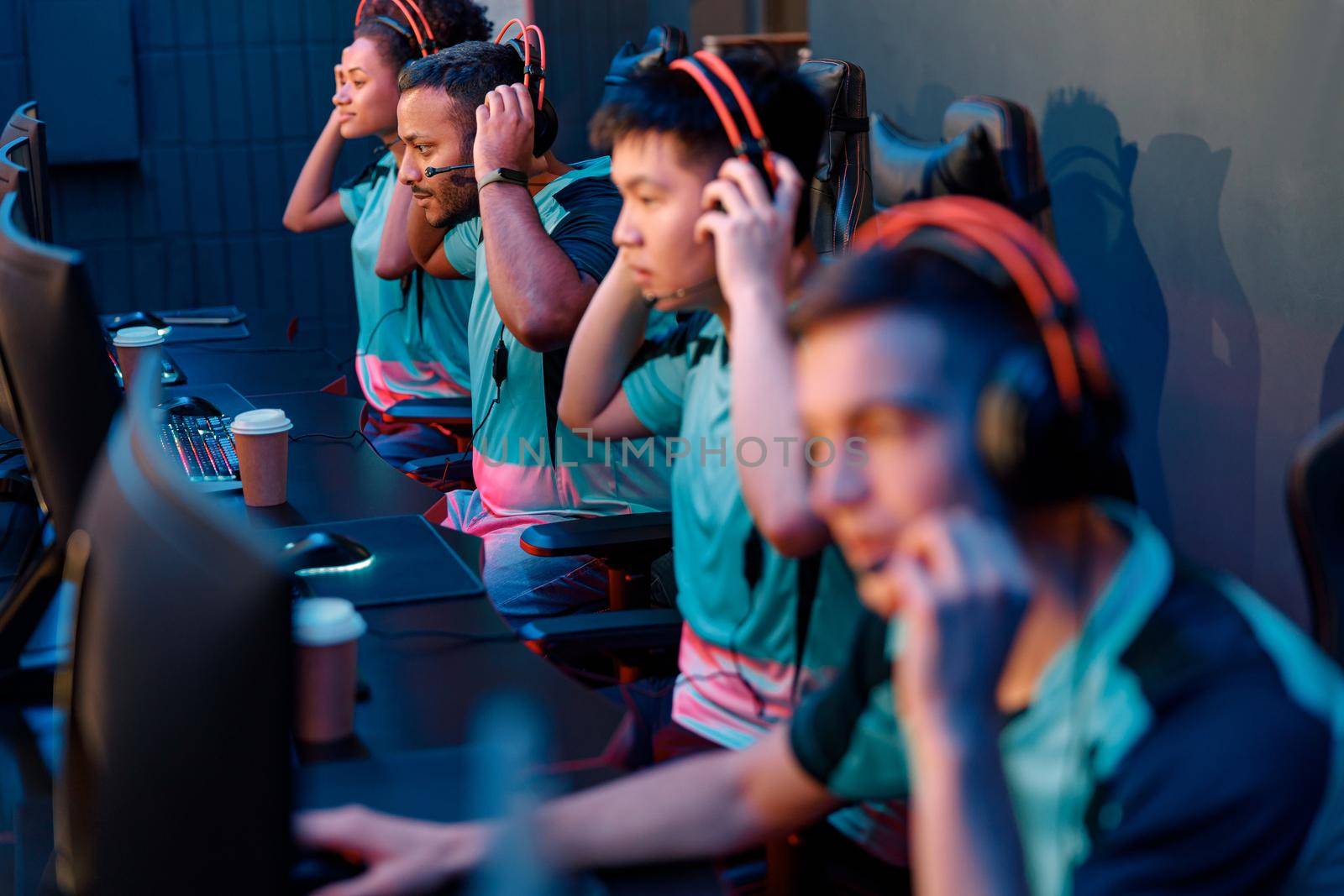 Group of three men and one woman sitting at computers putting on headphones and starting playing game in cyber club