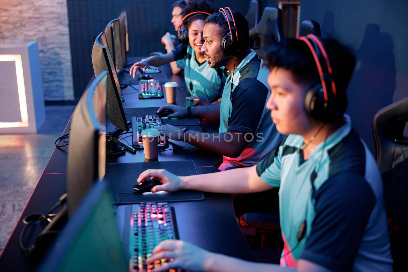 Group of multiethnic cybersport players in headsets sitting in front of computers and playing video games online in internet cafe