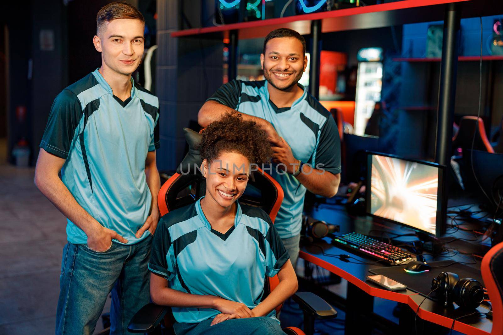 Happy African female gamer sitting on gaming chair with her teammates on background in contemporary esports club