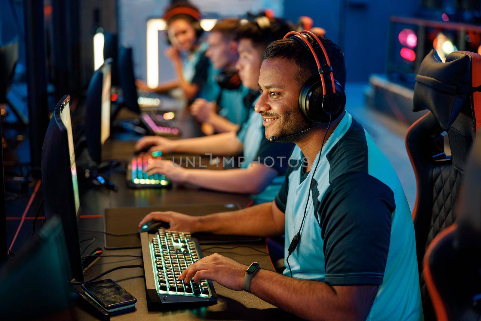 Happy cybersport gamer playing online game while sitting with other team members in front of PC monitors in computer club