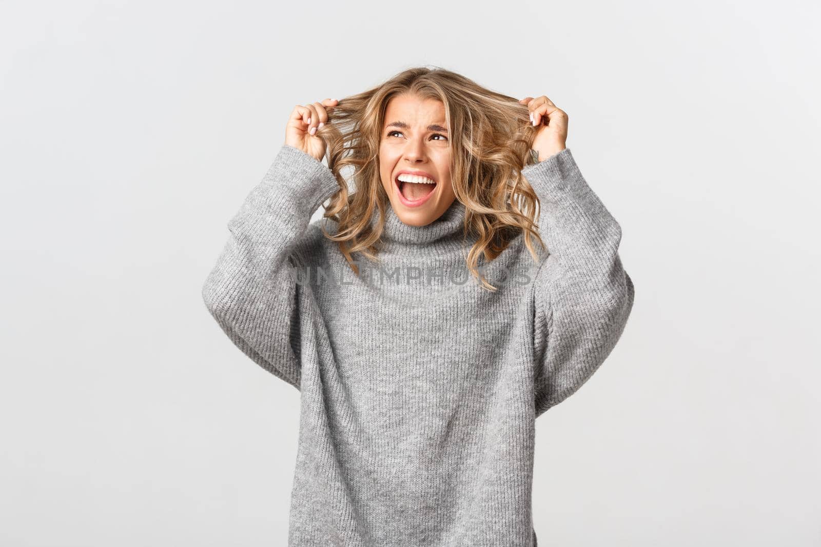 Image of nervous blond woman in panic, ripping hair on head and screaming alarmed, standing distressed against white background.