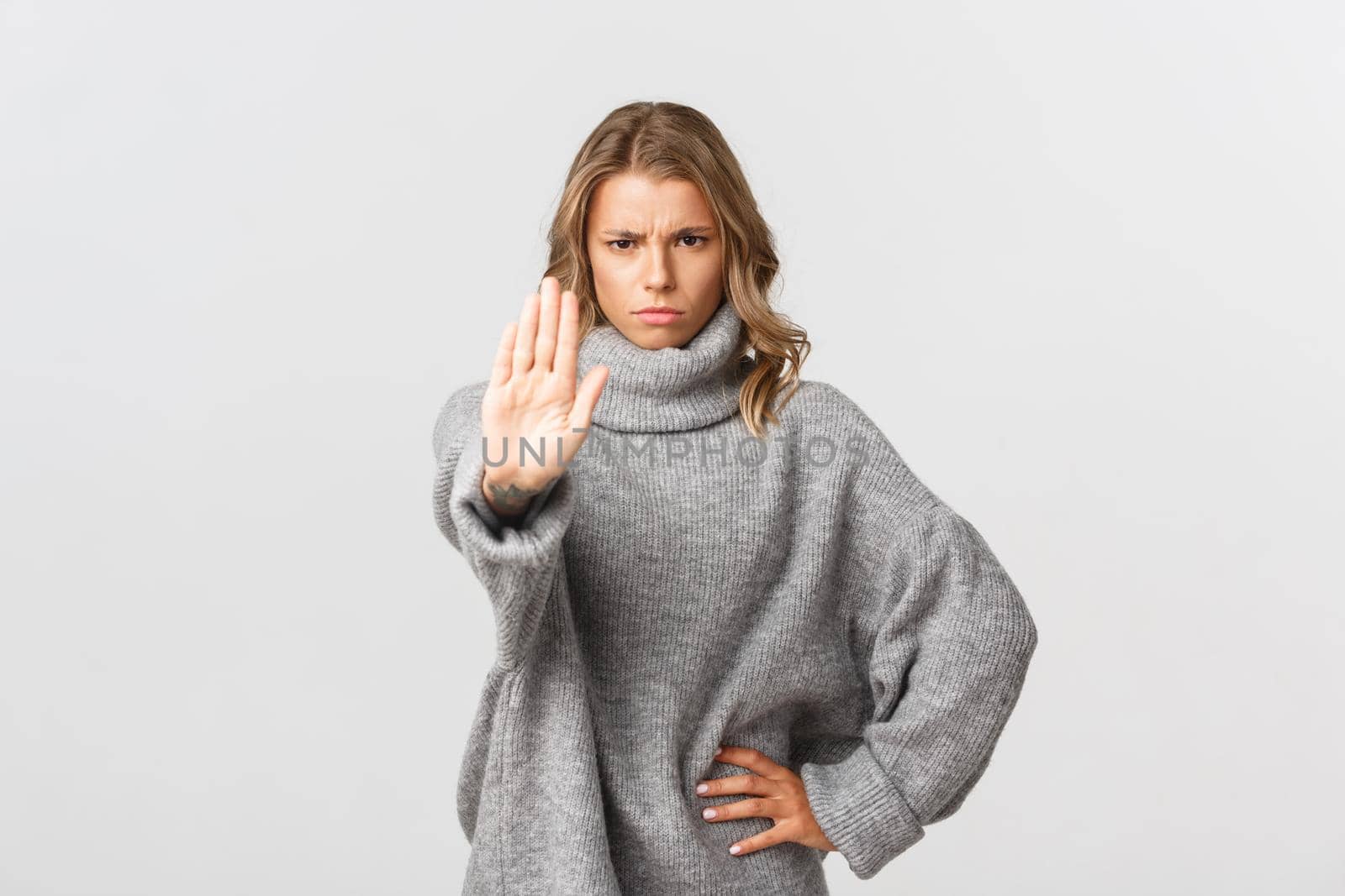 Serious confident woman in grey sweater, extend one arm and telling to stop, prohibit action, frowning disappointed, standing over white background.