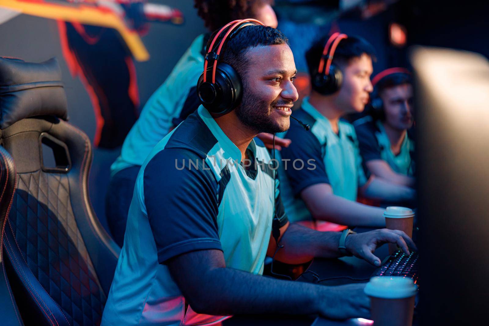 Happy professional cybersports gamer wearing headphones looking at PC screen and smile during esports tournament in gaming club