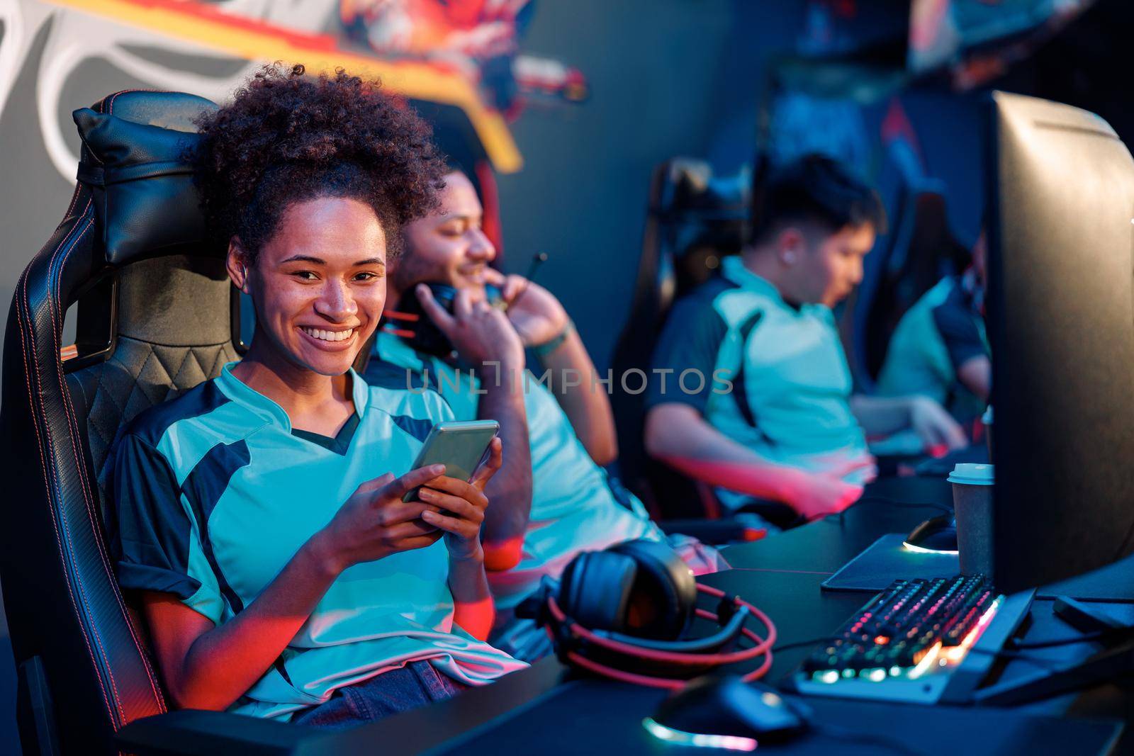 Young female professional cybersport gamer playing mobile game by smartphone on e-sports tournament online in colorful neon lights room