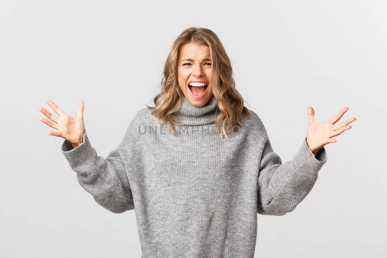 Image of distressed young woman screaming and shaking hands, standing emotional against white background.