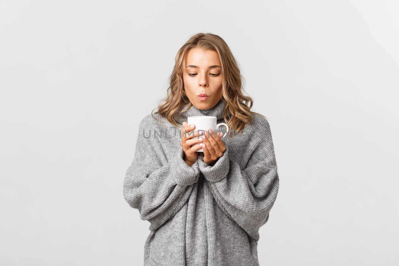 Image of attractive blond girl drinking hot tea or coffee, standing over white background.