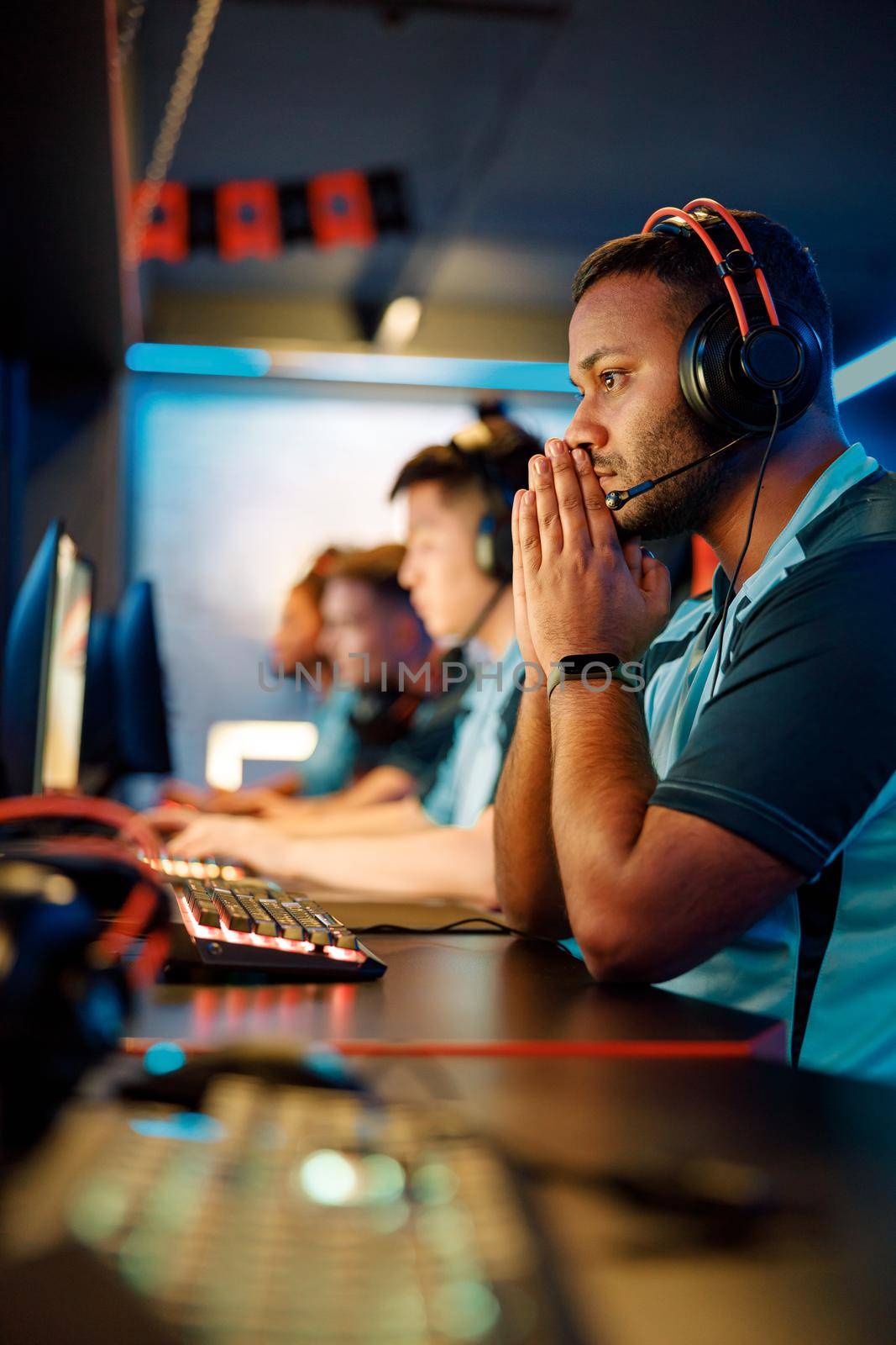 Serious young man in headset focused on video game while sitting at modern computer in internet cafe