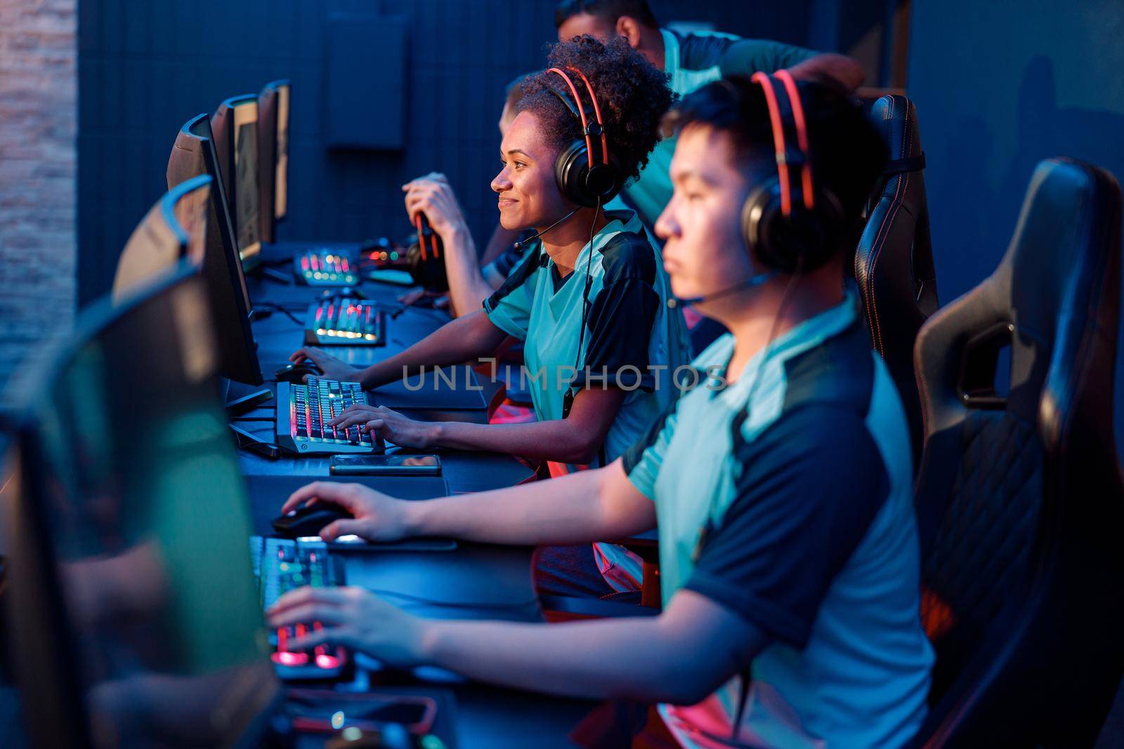 Selective focus on happy young woman sitting together with esports players and playing video game in internet cafe