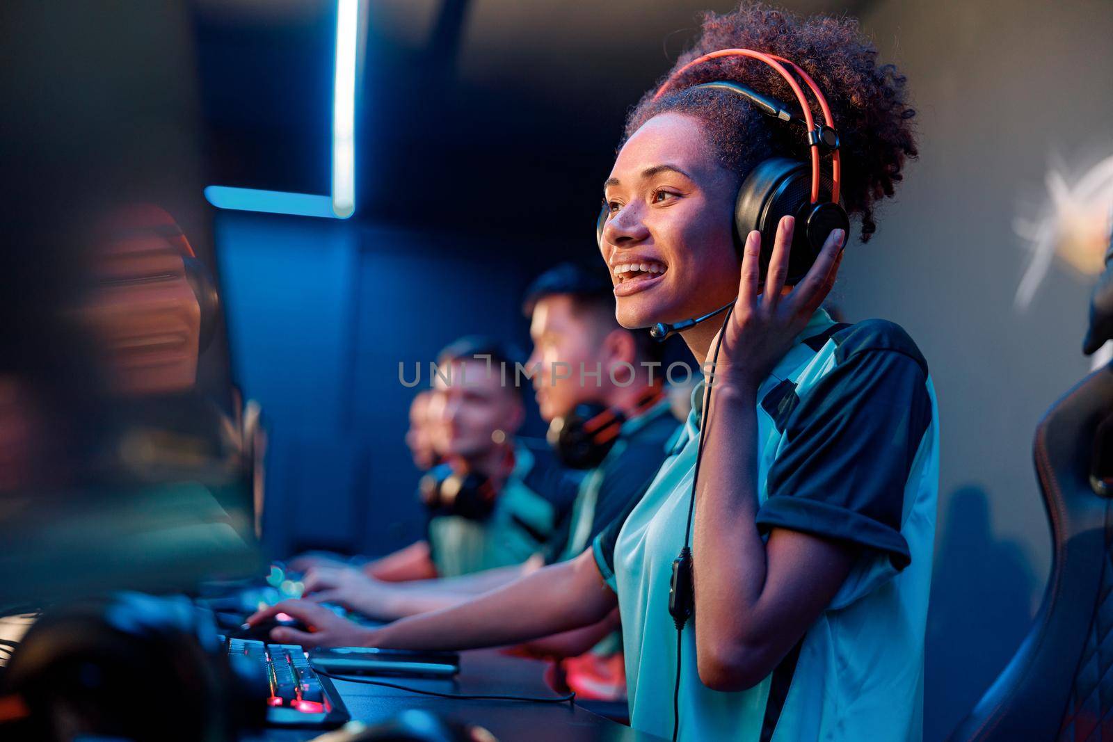 Happy African female gamer wearing headphones looking at PC screen and smile during esports tournament in gaming club