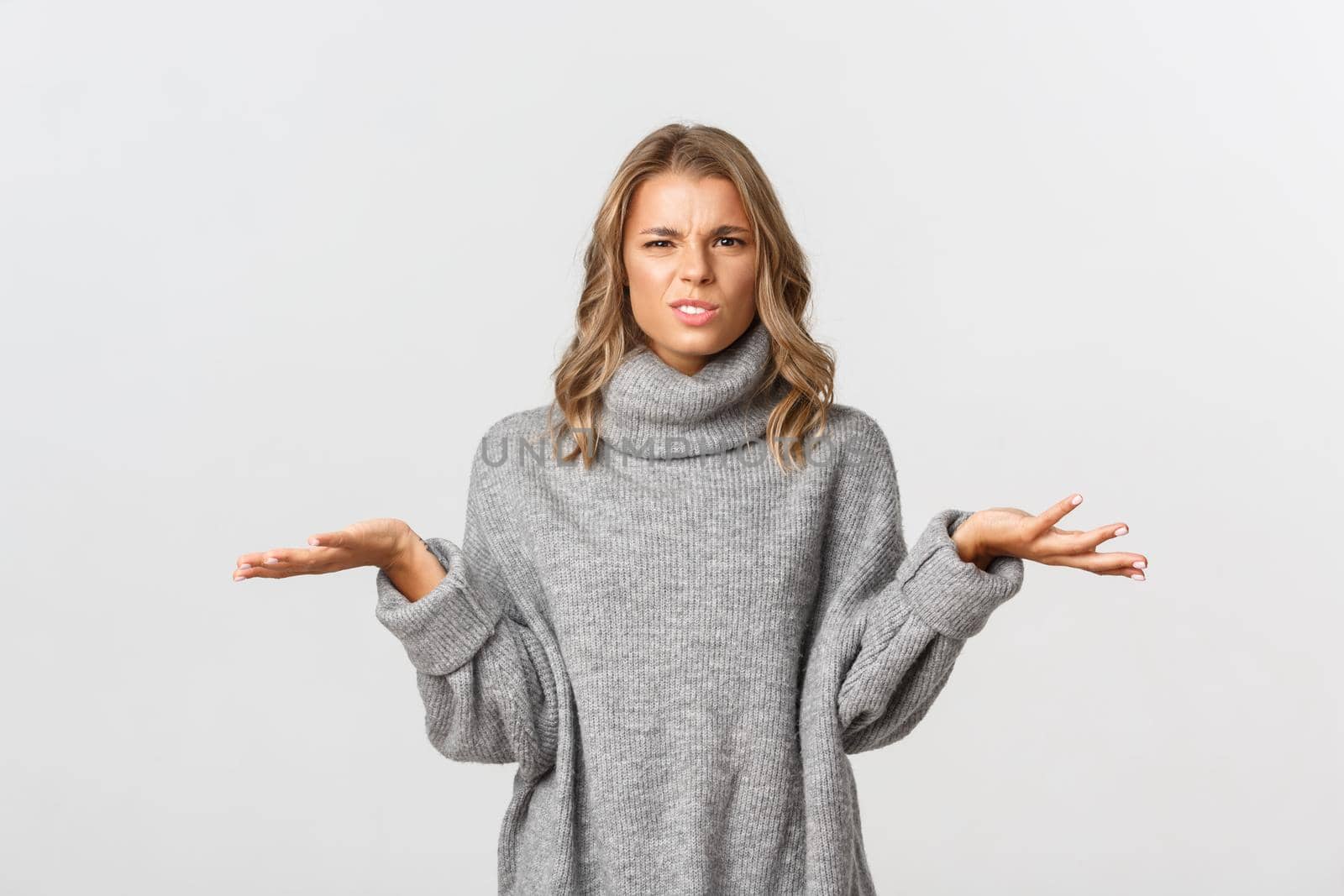Portrait of confused blond woman grimacing puzzled and shrugging, dont know whats happening, standing over white background.