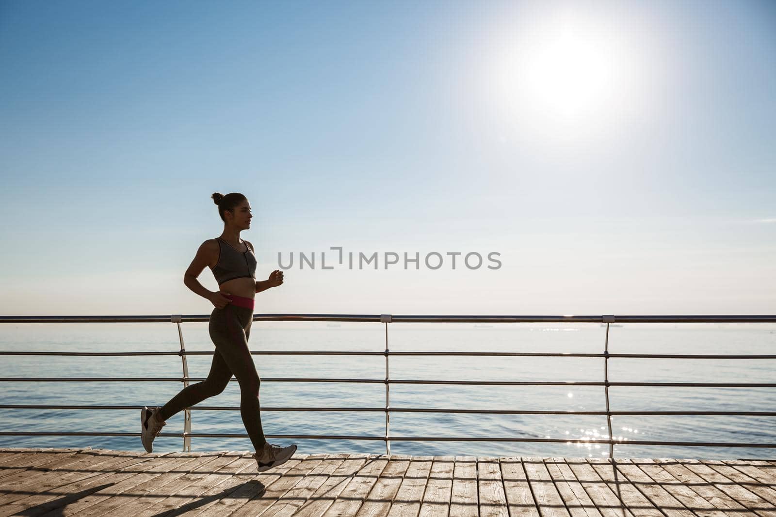 Image of attractive sportswoman jogging alone near the sea. Fitness woman running along seaside.