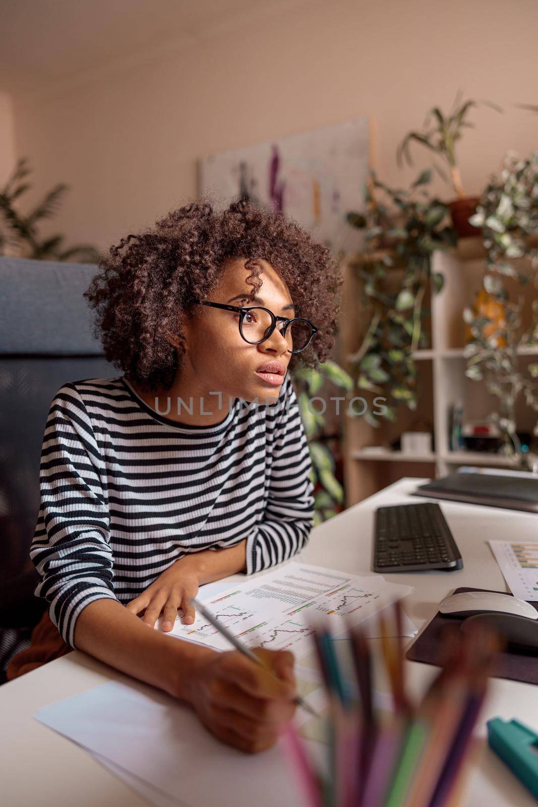 Serious multiethnic lady in glasses sitting at the table with documents and taking notes