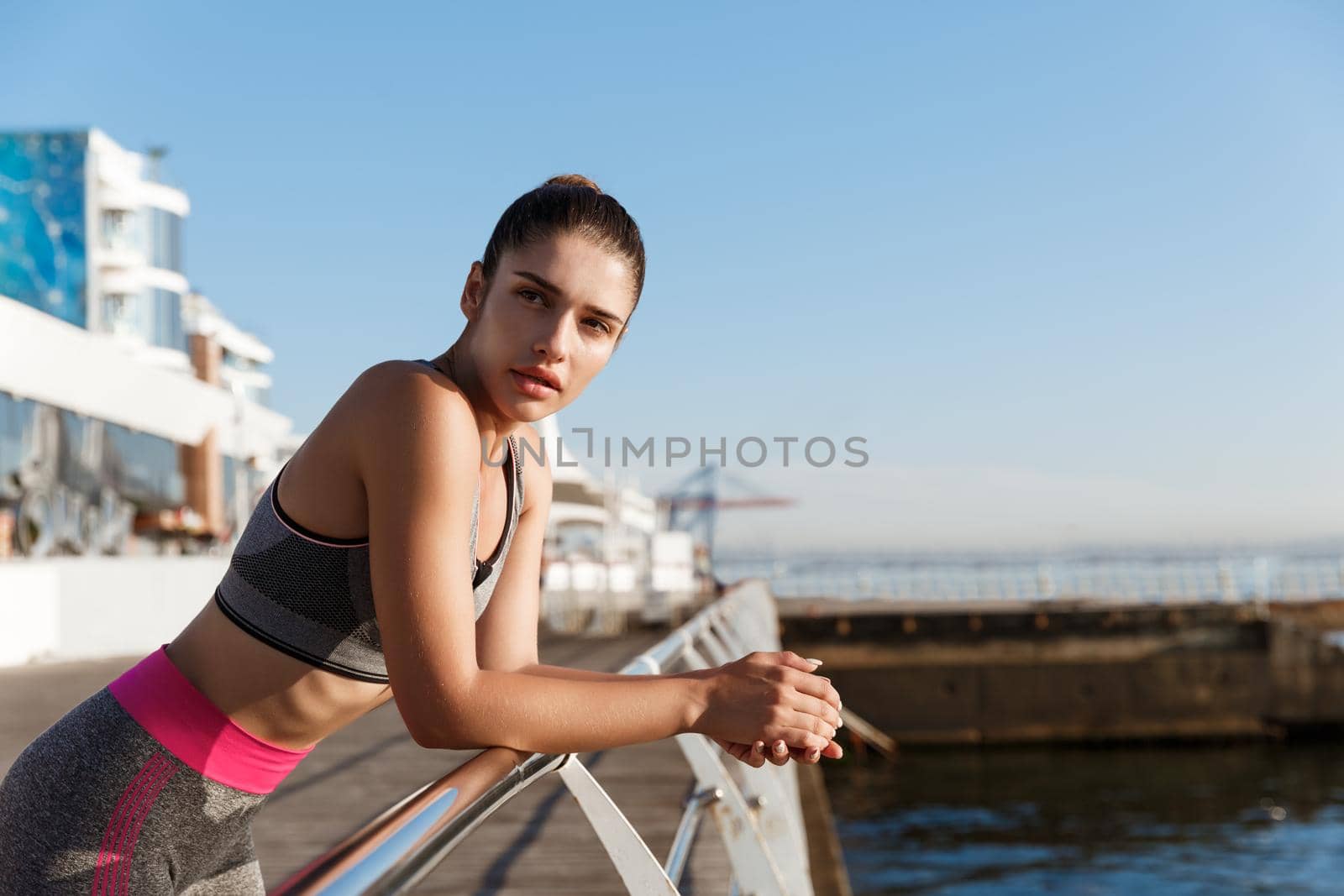 Close-up of attractive female athlete leaning on a handrail and looking at the sea, finish workout on the seaside promenade.