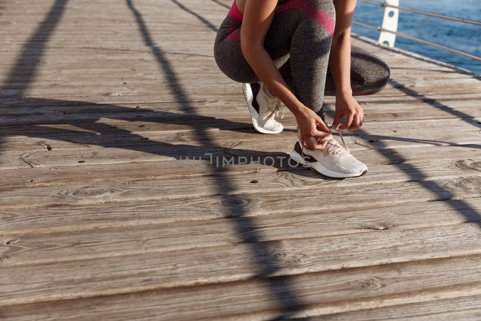 Cropped shot of fitness woman tying her shoelaces, prepare for jogging on the seaside promenade.