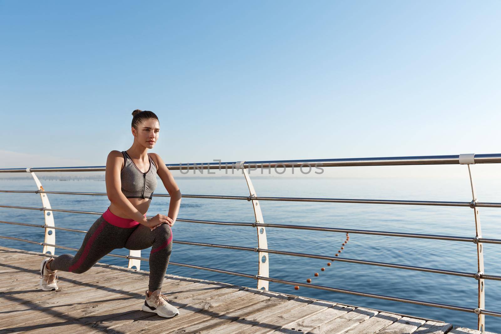 Outdoor shot of smiling fitness woman stretching and working out on the seaside promenade.