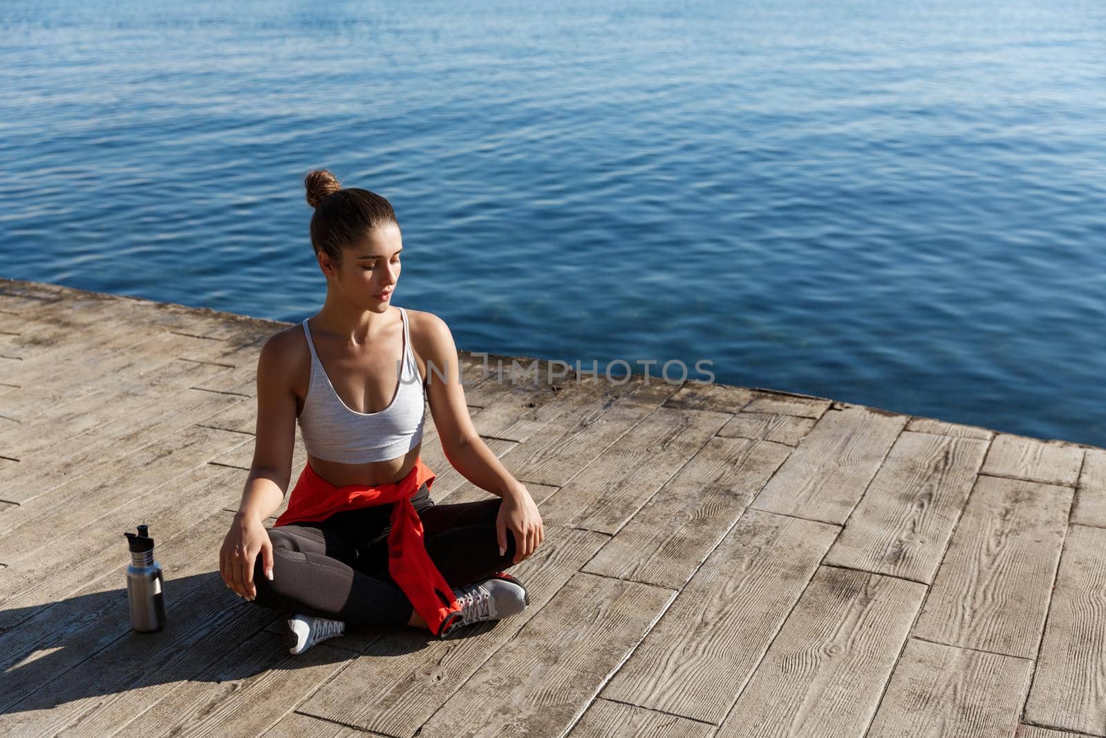 High angle shot of beautiful relaxed woman having yoga training near the sea, meditating on a pier by Benzoix