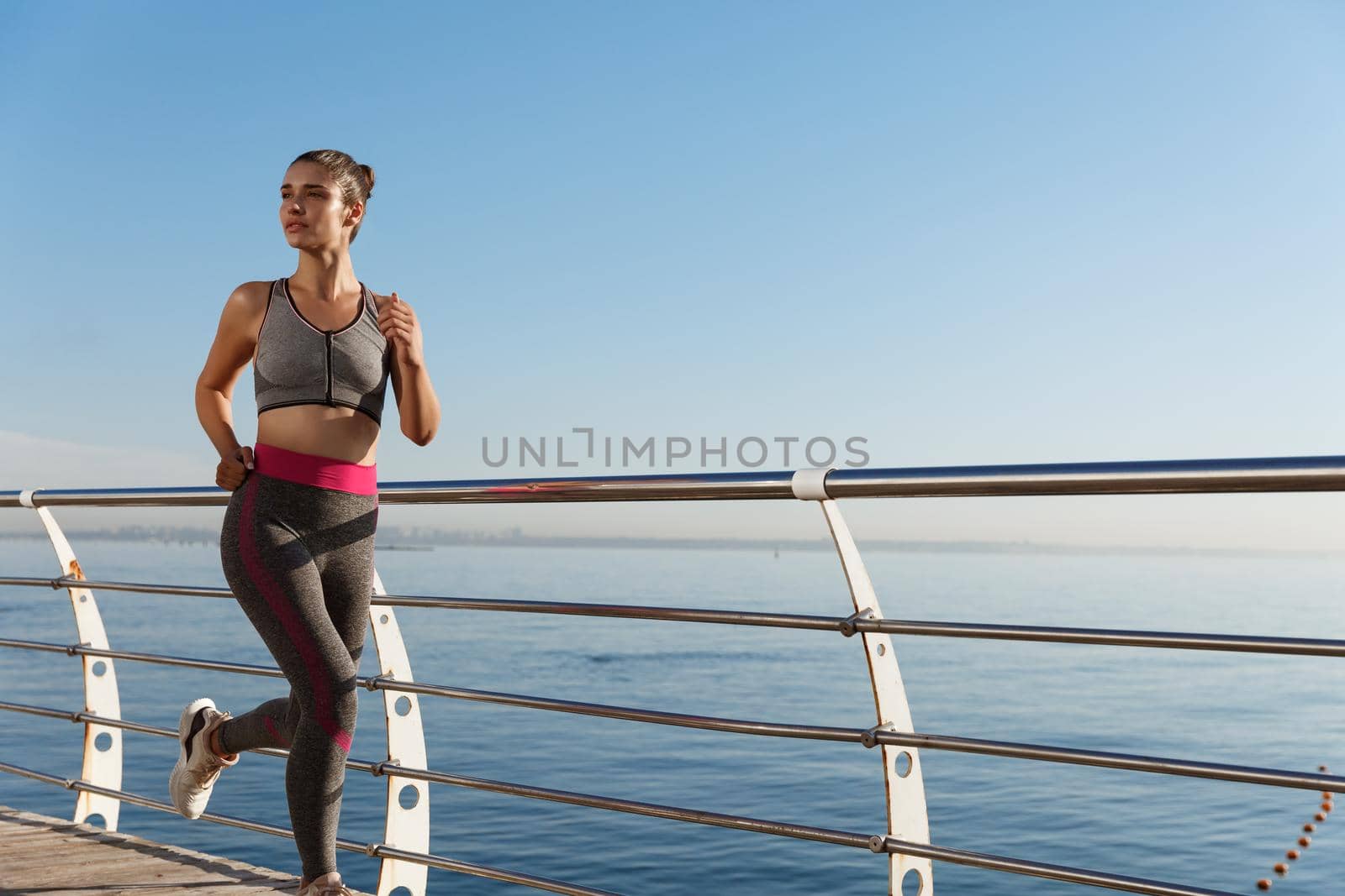 Outdoor shot of attractive fitness woman in sport clothing, jogging and training near sea.