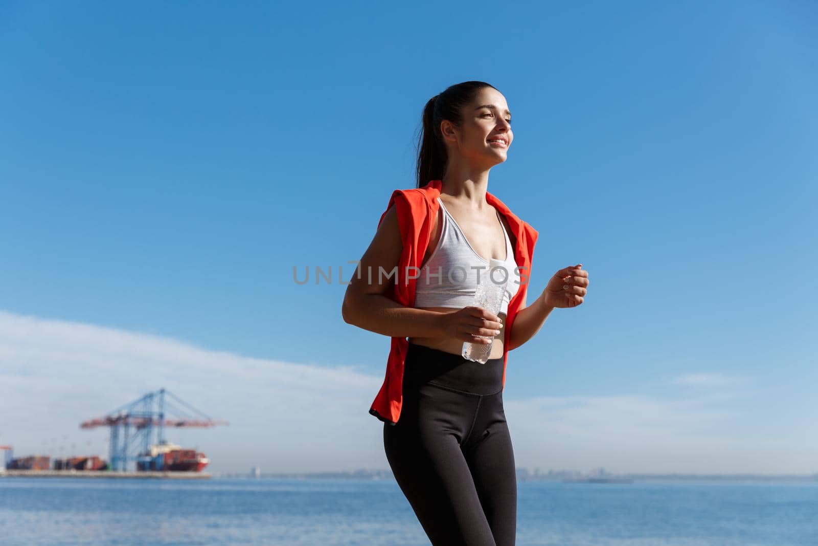 Low angle shot of happy woman running on seaside promenade. Sportswoman jogging in the morning on fresh air by Benzoix