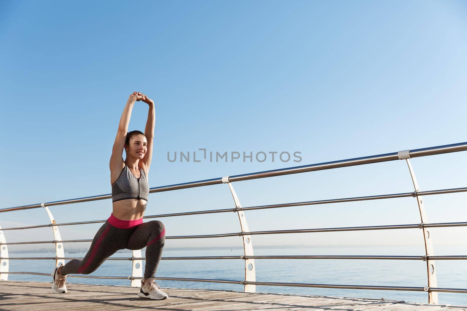 Low angle shot of healthy attractive fitness woman stretching legs and hands, workout alone near the sea. Girl warming-up before run by Benzoix