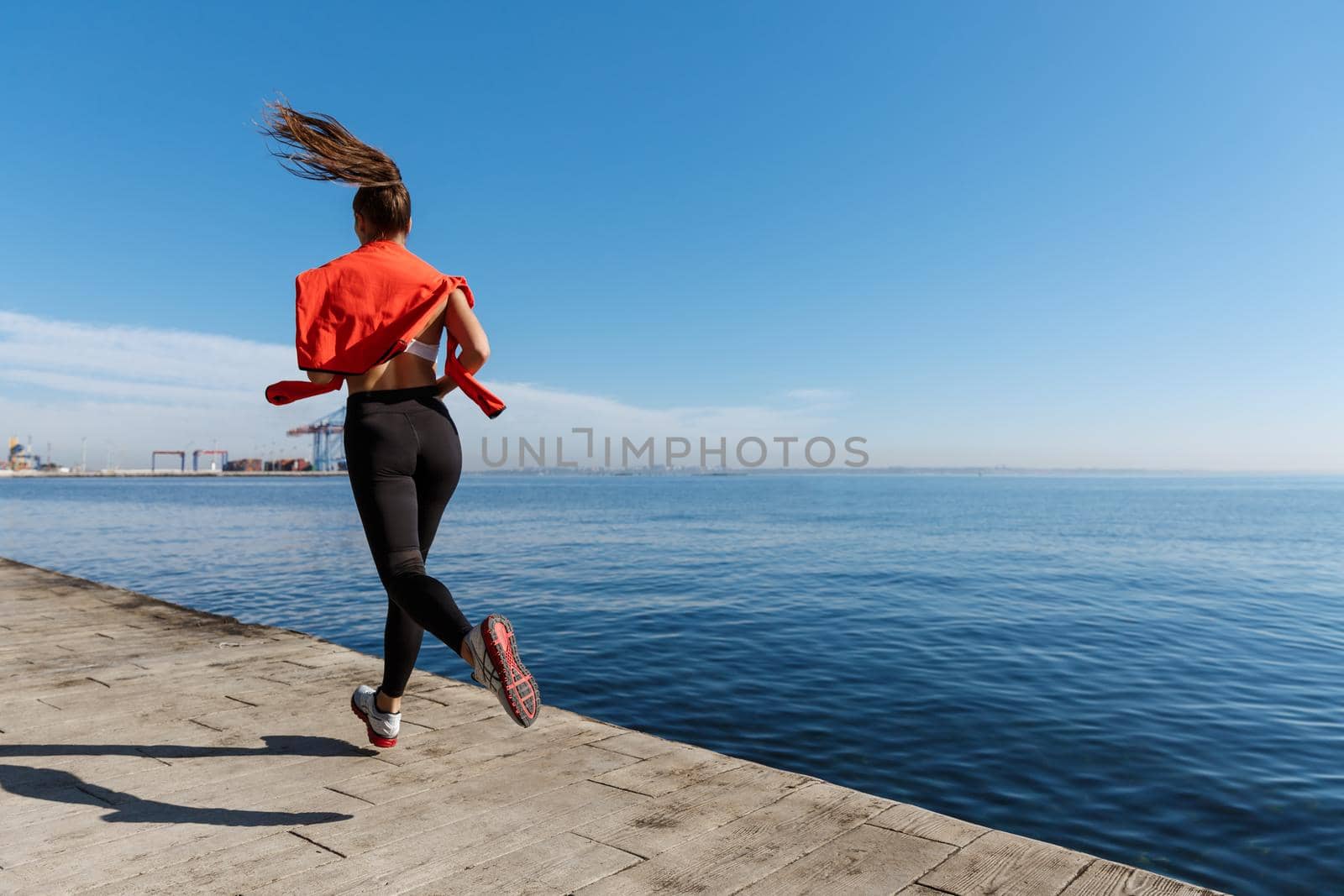 Rear view of sportswoman running along the seaside promenade. Fitness woman jogging near sea.