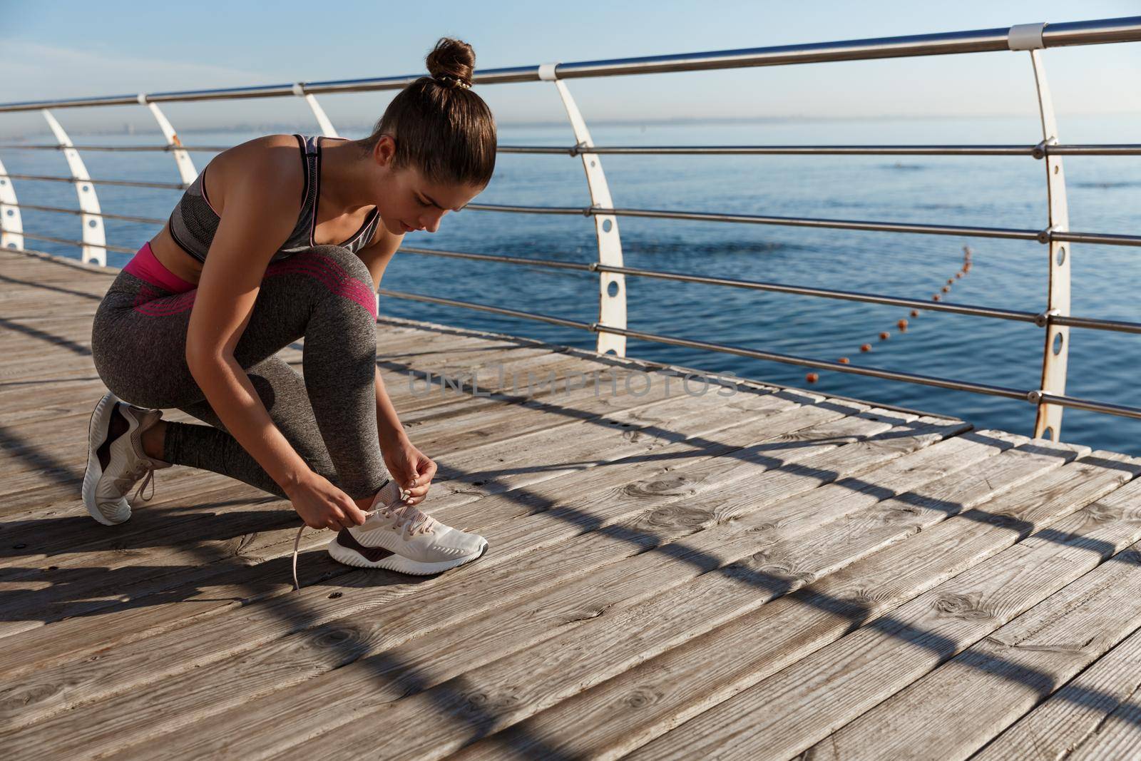 Young attractive fitness woman tying her shoes, jogging on the seaside promenade.