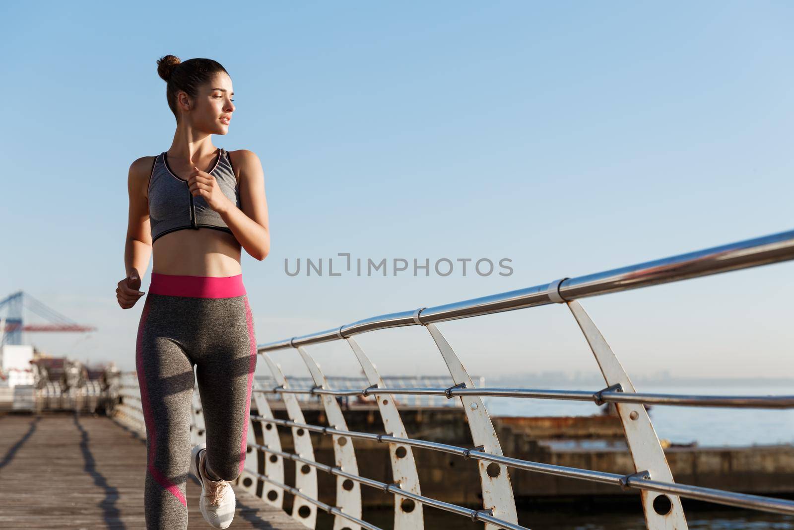 Portrait of young healthy woman jogging on the seaside promenade, running and looking at the sea thoughtful. Runner workout outdoors, training alone.