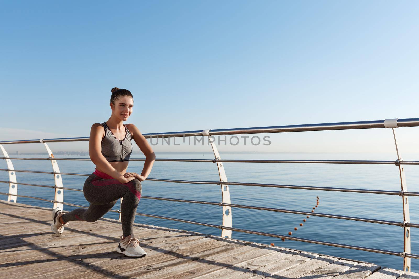 Outdoor shot of smiling fitness woman stretching and working out on the seaside promenade by Benzoix