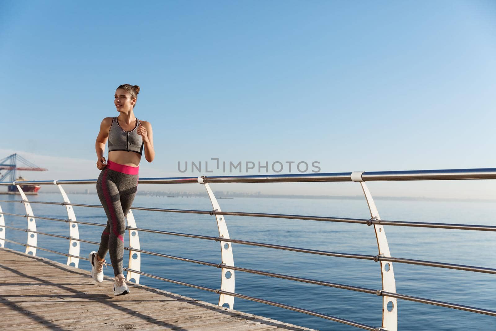 Image of young healthy sportswoman jogging near seaside. Fitness girl running and working out on pier.