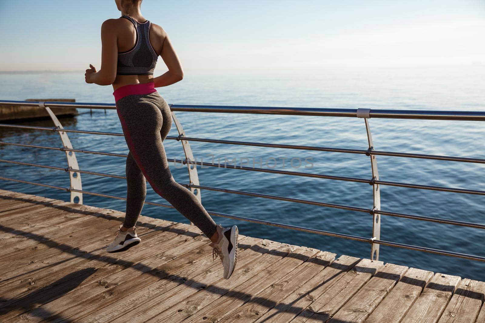 Cropped rear shot of fitness woman jogging on a pier, workout alone.