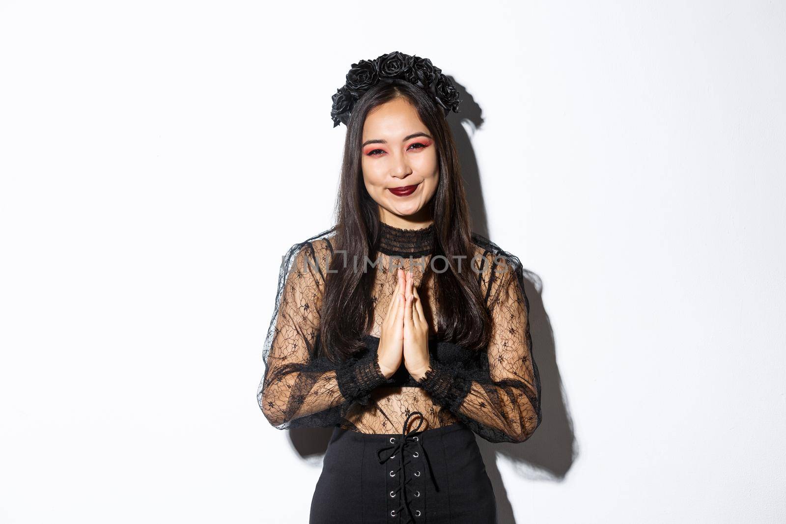 Image of happy and grateful young asian woman in gothic lace dress clasp hands together to say thank you, smiling thankful and standing over white background.