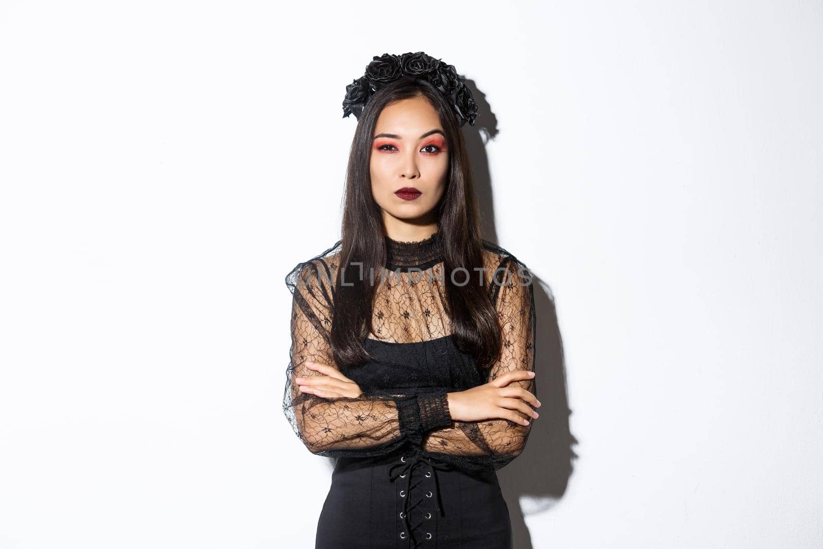 Skeptical young asian woman in witch or widow costume looking doubtful. Female dressed-up for halloween party, wearing black lace dress and wreath.