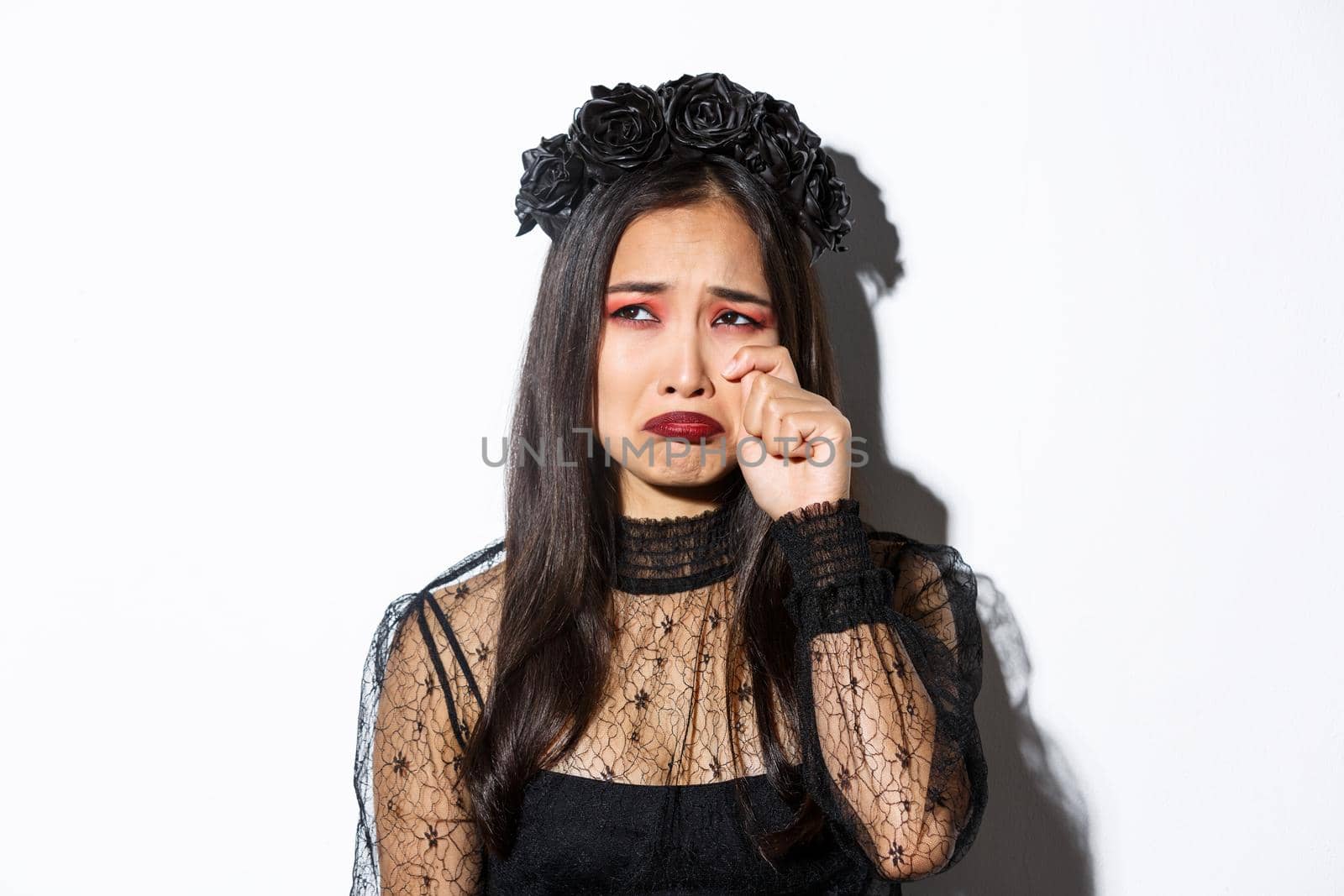 Close-up of young asian woman in witch costume crying and looking miserable, feeling sad, standing over white background by Benzoix