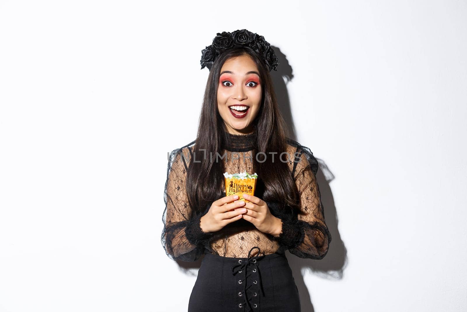 Beautiful asian girl smiling happy, holding sweets, wearing witch costume on halloween, enjoying trick or treating by Benzoix