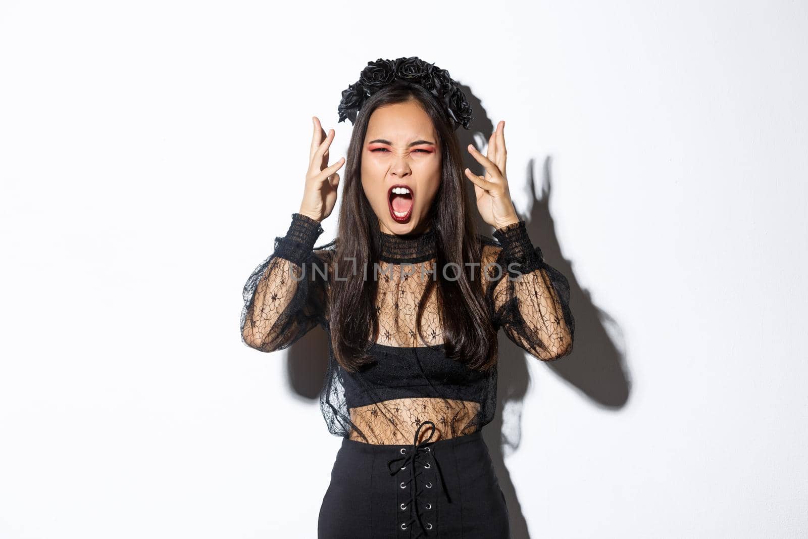 Image of angry asian woman in witch costume yelling at someone, looking mad, losing temper and screaming, standing over white background pissed-off.